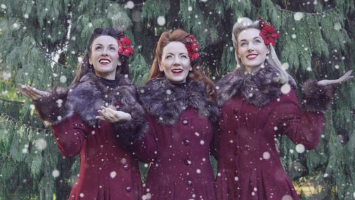 3 women in red coats with flowers in their hair.